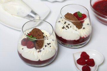 Cooking cream cheese dessert with raspberry jelly. The ingredients are laid out on the table surface. Decorated with cookies, raspberries and mint.