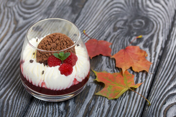 Dessert made from cream cheese with raspberry jelly. Decorated with cookies, raspberries and mint. Dried autumn maple leaves are all around.