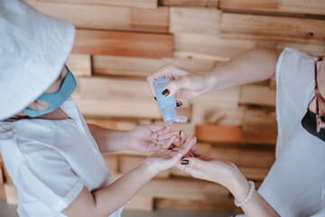 Asian mother and daughter using wash hand sanitizer gel bottle on the city street.