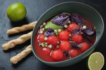 Green bowl of gazpacho cold soup made of red tomatoes and watermelon, studio shot on a black stone surface