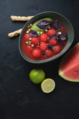 Bowl of watermelon and tomato gazpacho soup, top view on a black stone background, vertical shot with copyspace