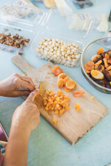 Young woman making Turkish dessert (asure) in the kitchen. Traditional Sweet Ashura, Ashura or Noah's Pudding. Woman cutting dried fruit for Ashura preparation.