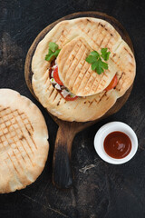 Rustic wooden serving board with doner kebab pitas, flatlay on a dark brown stone background, studio shot