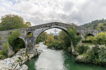 Fototapeta na wymiar Roman bridge in the city of Cangas de Onis, Spain with the cross of victory hanging from the arch.