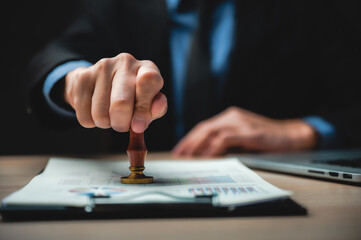 person's hand stamping with approved stamp on business marketing document at desk in modern office