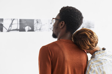 Graphic portrait of mixed-race couple embracing while looking at paintings at modern art gallery...