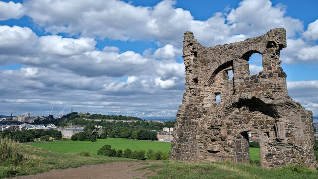 Summer photo of Saint Antony's Chapel ruins in Holyrood Park. With Edinburgh Skyline and famous landmarks in the background, including Calton Hill and the city's palace and gardens in Scotland UK