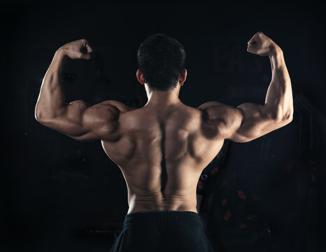 Muscular model young man on dark background. Strong brutal guy showing his biceps triceps, flexing his muscles. back abs. Sport workout bodybuilding healthy lifestyle concept.