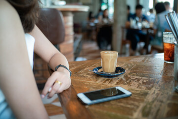 Fototapeta na wymiar Women hand use smartphone drink hot latte coffee sitting in cafe