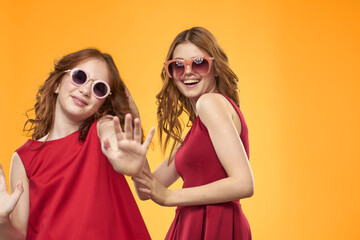 Happy sisters in red dresses on a yellow background are having fun and gesticulating Copy Space