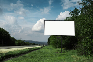 Empty billboard for advertising poster near asphalting road and green forest, on background of blue sky.