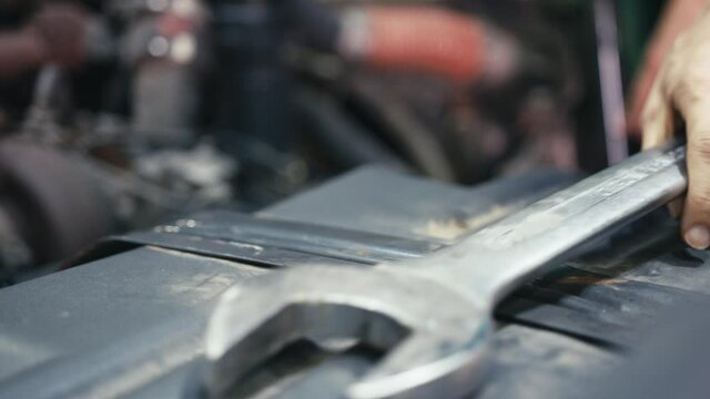 Car mechanic placing a large wrench aside when working on a truck engine. Slow motion.