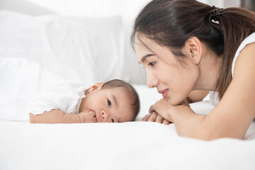 Obraz na płótnie Canvas Beautiful asian mother and baby are playing on white bed and looking at each other. Happy asia mother and infant lying on bed at home.