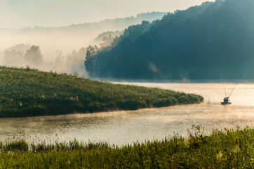 thick morning fog in the summer forest near the reservoir. fishermen on a boat - 384809118