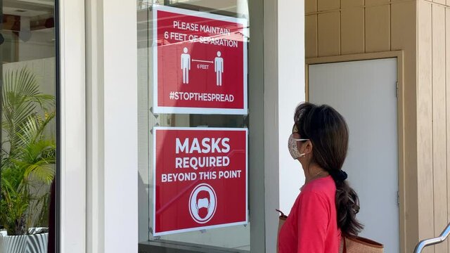 Attractive Woman Wearing Covid Mask Reads Sign Instructing Social Distancing And Masks 