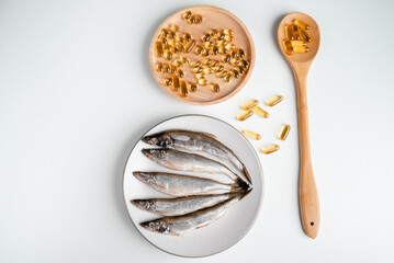 Omega 3 pills on spoon, fish oil and fish on white background. 
Health and immunity strengthening fish oil capsules. 
Healthy food
