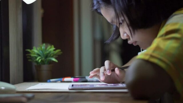 Asian children writing and using smartphone to doing homework at home. Happy Thai Kid drawing and painting with color pencil At night. Education concept.