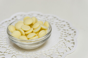 Many white chocolate pellets in a glass bowl on white background