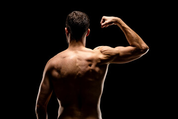 Strong muscular man showing biceps back view, isolated on black background.