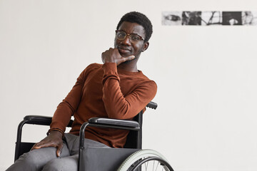 Minimal portrait of young African-American man using wheelchair and looking at camera while posing...