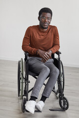 Minimal full length portrait of young African-American man using wheelchair and looking at camera...