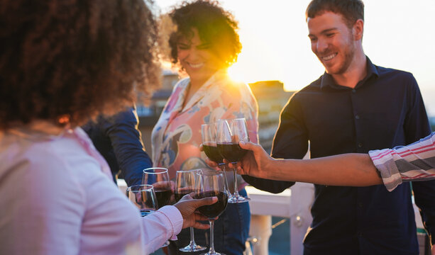Happy multiracial people cheering with wine outdoor at sunset - Young friends enjoy dinner together at home