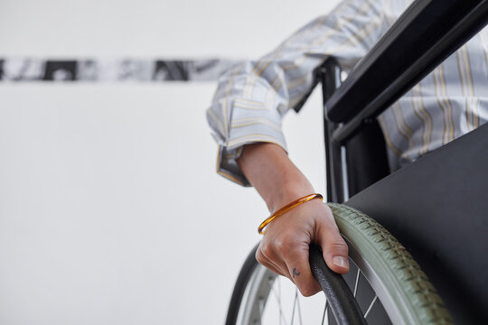 Close up of unrecognizable young woman pushing wheels of wheelchair against white background, copy space