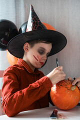 Happy teen boy in costume preparing for the Halloween celebration drawing a pumpkin. Halloween...