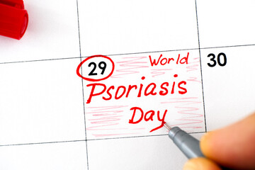 Woman fingers with pen writing reminder World Psoriasis Day in calendar