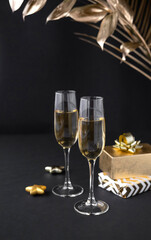 Two glasses of champagne over black background and golden Christmas decoration. Holiday decorations on dark table.