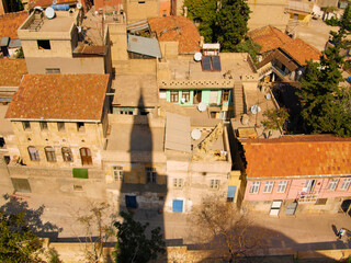 Fototapeta na wymiar A bird view of an old tumbledown slum neighbourhood, dirty stone, concrete and mud facades. Poor street view and a mosque minaret shadow on the roofs in the middle east town.