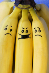 Social distancing concept. Bunch of bananas with cute faces symbolising social distancing during the pandemic. One banana is wearing a mask and the others are scared of being close to him and catching