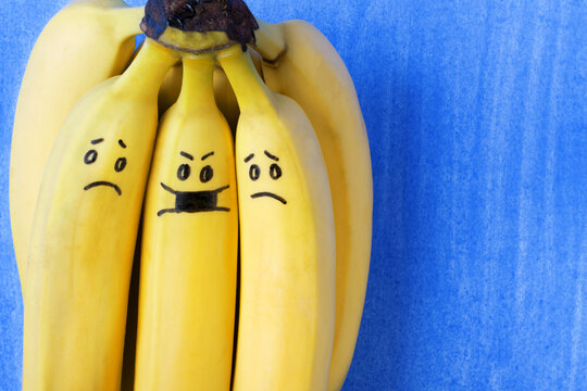 Social distancing concept. Bunch of bananas with cute faces symbolising social distancing during the pandemic. One banana is wearing a mask and the others are scared of being close to him and catching