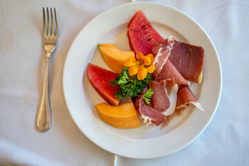 Arrangement of Delicatessen Cold Cuts with charcuterie, melon and watermelon decorated with orange flower and parsley. Soft focus background