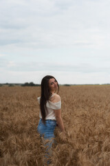 Naklejka na ściany i meble Happy woman in a wheat field is laughing. Brunette with ears of wheat.