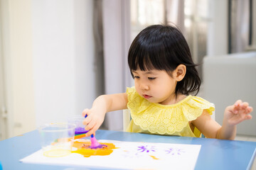 The baby girl is painting watercolor into paper. - 384820791