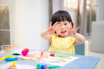 happy Toddler painting watercolor with her hand. smiley baby girl with painted hand. - 384821101