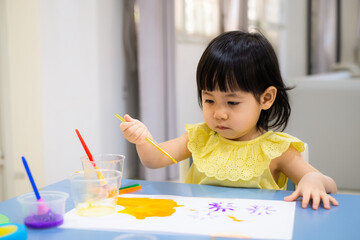 The baby girl is painting watercolor into the paper. - 384821151
