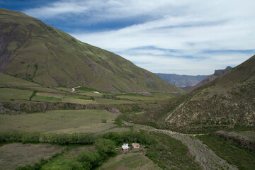 Fototapeta premium Rural landscape. The green valley and hills. View of a small farm house in the field surrounded by mountains.