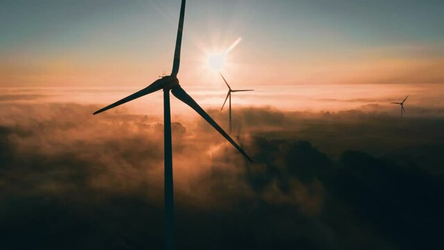 Wind turbine at sunrise in heavy fog. Wind farm generating green energy