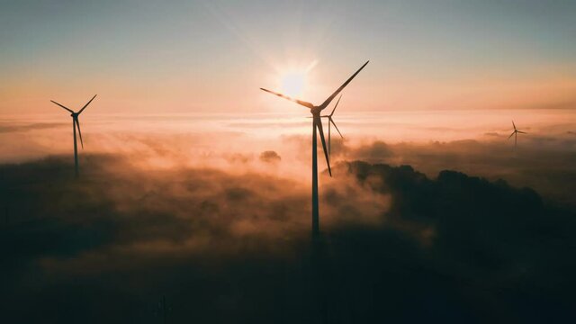 Wind turbine at sunrise in heavy fog. Wind farm generating green energy