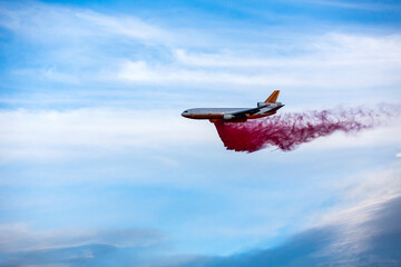 Fototapeta premium Emergency response tanker airplane drops fire retardant over a wildfire blue skies with clouds