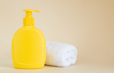 Fototapeta na wymiar Yellow unbranded dispenser bottle next to white towel on beige background