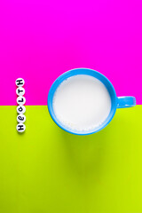 milk in blue cup and inscription HEALTH made of white medical pills on a bright pink and green  background