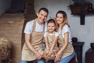 Concept of ceramic art and hobby. Happy family of three people making potter and using wheel circle. They sitting in cozy room or work place studio and working with raw and wet clay.