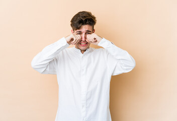 Young caucasian man isolated on beige background whining and crying disconsolately.