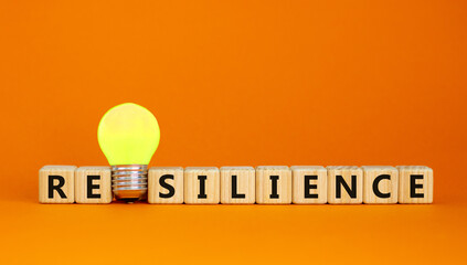 Wooden cubes with word 'resilience'. Yellow light bulb. Beautiful orange background. Business concept. Copy space.
