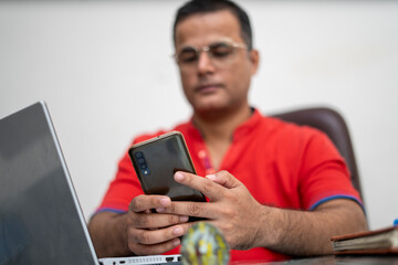 technology, remote job and lifestyle concept - happy indian man in glasses working on phone.