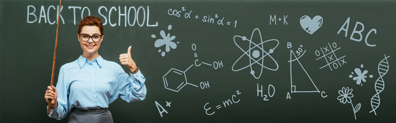 panoramic shot of chemistry teacher with pointing stick showing thumb up near chalkboard with back to school lettering and illustration