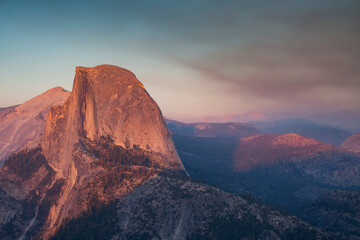 Sunset with alpine glow on the iconic Half Dome just beyond Glacier Point Road in Yosemite National Park. The sky is filled with smoke and haze from a wildfire burning inside of the park